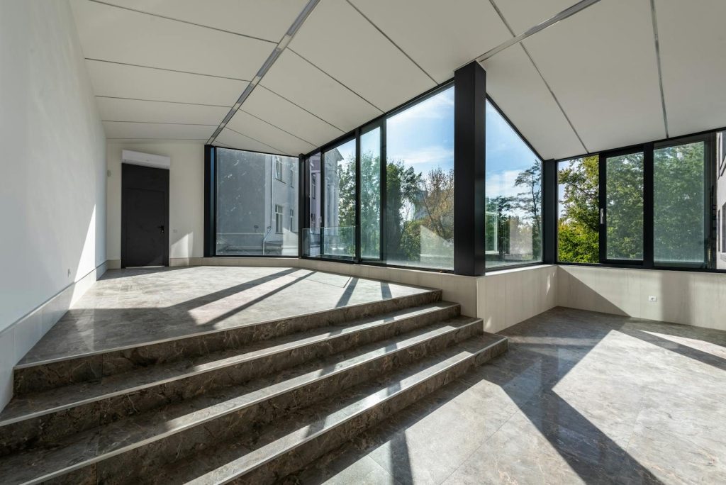Spacious modern room with large glass windows and marble steps, flooded with natural light.